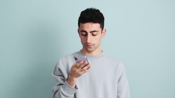 一位英俊的黑发男子站在工作室的蓝色背景下 在手机上记录着一条语音信息 — 图库视频影像