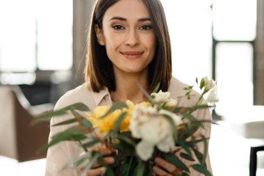 Gülümseyen orta yaşlı kadın, oturma odasını vazoda çiçek buketiyle süslüyor.