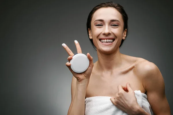 Mujer Sonriente Blanca Vestida Con Toalla Mostrando Crema Facial Aislada —  Fotos de Stock