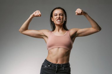 Beyaz kadın, gri arka planda izole edilmiş pazılarını gösterirken sütyen takıyor.