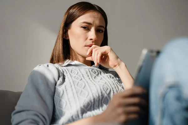 严重皱眉的中年妇女一边在家里的沙发上放松 一边用数码平板电脑 — 图库照片