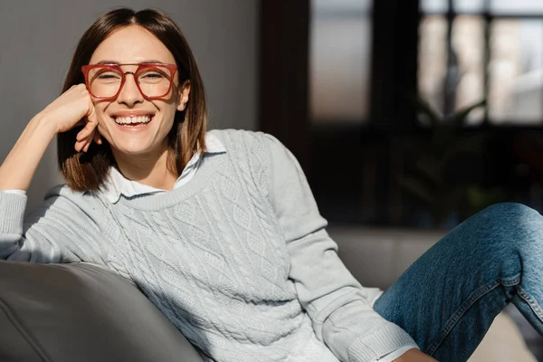 Mujer Joven Con Anteojos Riéndose Cámara Mientras Está Sentada Sofá — Foto de Stock