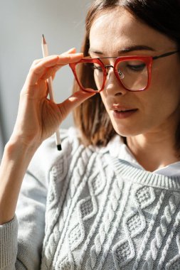 Süveter giymiş, elinde gözlük ve kalemle gülümseyen orta yaşlı bir kadın.