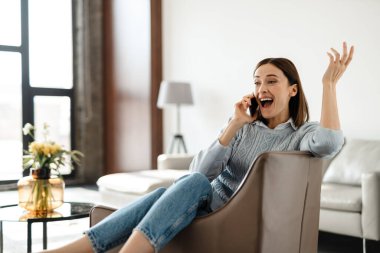 Sınıfta koltukta otururken cep telefonuyla konuşan heyecanlı genç bir kadın.