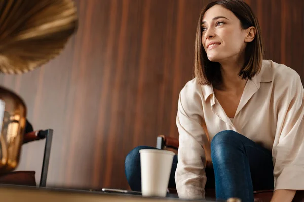 Joven Mujer Complacida Bebiendo Café Mientras Está Sentado Sillón Interior —  Fotos de Stock