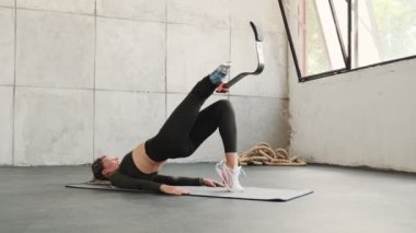 Bacak protezi olan güçlü bir kadın stüdyoda yoga minderi üzerinde egzersiz yapıyor.