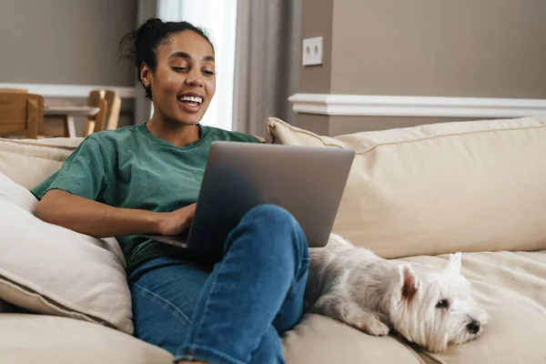 Wanita Kulit Hitam Tersenyum Menggunakan Laptop Sambil Duduk Dengan Anjingnya — Stok Foto