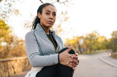 Odaklanmış Afrikalı Amerikalı sporcu kadın parkta çalışırken bacağını esnetiyor.