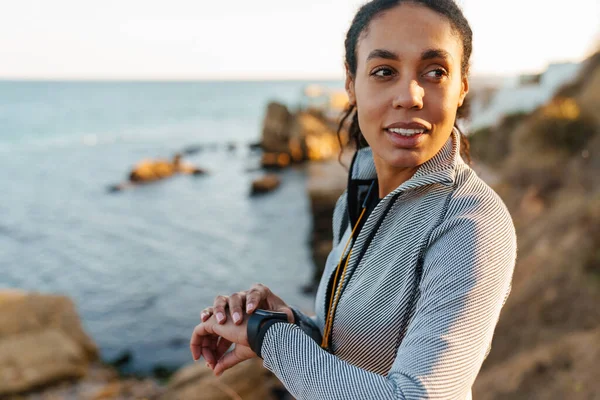 Sonriente Deportista Afroamericana Mirando Smartwatch Mientras Está Pie Playa — Foto de Stock