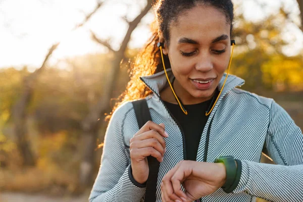 Szczęśliwa Afrykańska Sportowiec Amerykański Słuchawki Patrząc Smartwatch Parku — Zdjęcie stockowe