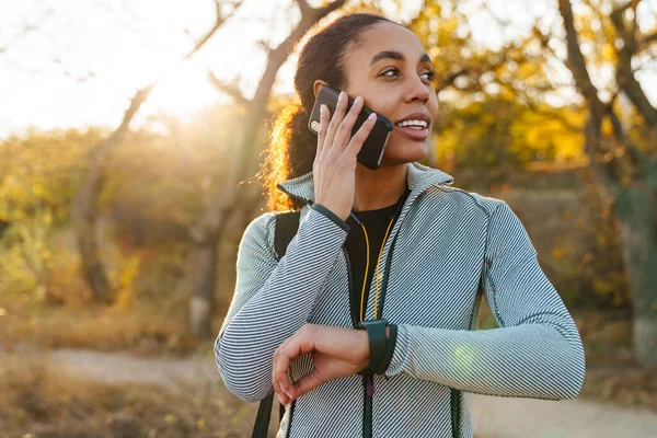Pleased African American Sportswoman Talking Cellphone While Using Smartwatch Park — 스톡 사진