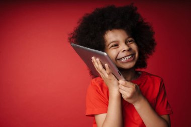 Kırmızı duvar arkasında tablet tutan mutlu Afrikalı bir çocuğun fotoğrafını çek.