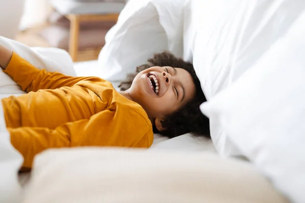 Black curly boy laughing while making fun in bed at home