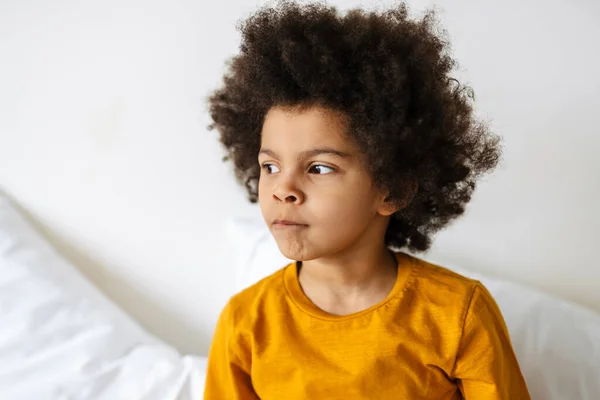 Schwarz Lockiger Junge Schaut Beiseite Während Hause Bett Sitzt — Stockfoto