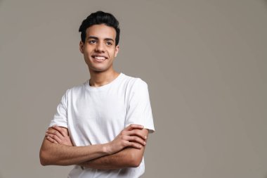 Esmer, tişörtlü, gülümseyen ve gri arka planda tek başına duran esmer bir adam.