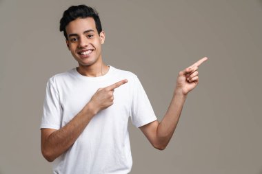 Esmer, tişörtlü, gülümseyen ve parmağıyla işaret eden esmer bir adam gri arka planda soyutlanmış.