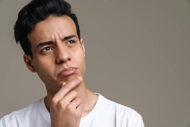 Tişörtlü dalgın, esmer bir adam gri duvarın arkasında dikiliyor.