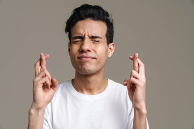 Gülümseyen esmer, tişörtlü adam gri duvar arkasında duruyor.