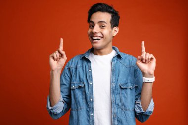 Esmer, tişörtlü, gülümseyen ve parmaklarını yukarı gösteren, kırmızı arka planda soyutlanmış bir adam.