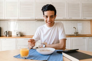 Genç İspanyol adam evde mutfakta kahvaltı yapıyor, masada oturuyor.