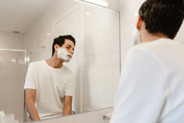 Genç İspanyol adam, içeride aynanın karşısında yüzünü tıraş ediyor.