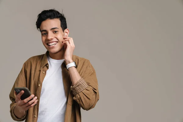 Brunett Hispanic Man Ler När Använder Mobiltelefon Och Hörlurar Isolerade — Stockfoto
