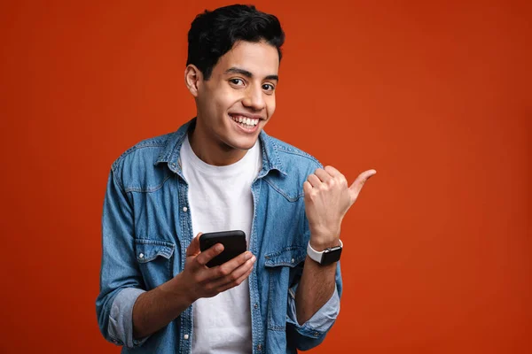 Uomo Sorridente Puntando Dito Parte Utilizzando Cellulare Isolato Sfondo Rosso — Foto Stock