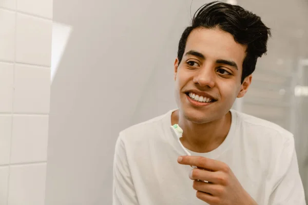 Glimlachende Jonge Latino Man Poetsen Tanden Bij Badkamer Spiegel — Stockfoto