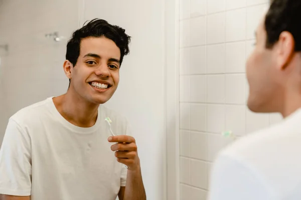 Улыбающийся Молодой Латиноамериканец Чистит Зубы Перед Зеркалом Ванной — стоковое фото