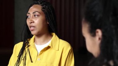 Memnun bir Afro-Amerikalı esmer iş kadını konferans sırasında ofisinde oturmuş ortaklarıyla konuşuyor.