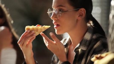 Gözlüklü beyaz bir iş kadınının yakın plan görüntüsü iş arkadaşlarıyla birlikte ofiste pizza yiyor.