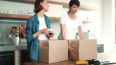 Yeni eve taşındıktan sonra kutuları açarken öpüşen ve birbirlerine bakan birkaç mutlu kız.