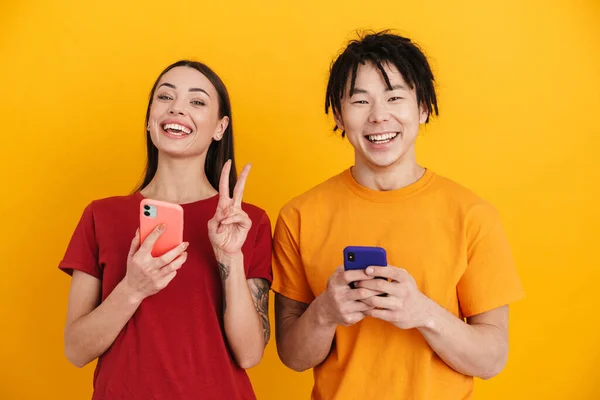 Jovem Casal Multirracial Gesticulando Sinal Paz Usando Telefones Celulares Isolados — Fotografia de Stock