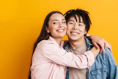 Sarı duvarın üzerinde izole bir şekilde fotoğraf çekilirken gülümseyen ve sarılan genç çift.