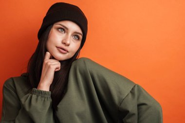 Uzun saçlı, kırmızı arka planda duran şapkalı, dalgın, esmer bir kadın.