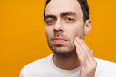 Üzgün, orta yaşlı esmer bir adamın yüzünü incelerken, sarı arka planda izole edilmiş.