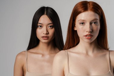 Beyaz duvarın üzerinde poz veren temiz, genç yüzlü iki güzel kızın stüdyo portresini kapat.