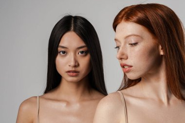 Beyaz duvarın üzerinde poz veren temiz, genç yüzlü iki güzel kızın stüdyo portresini kapat.