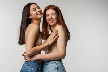 Beyaz duvarın üzerinden izole edilmiş kameraya sarılıp gülen iki kadın.