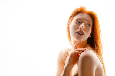 Genç Avrupalı kızıl kadın beyaz duvarın üzerinde poz veriyor ve yan bakıyor.