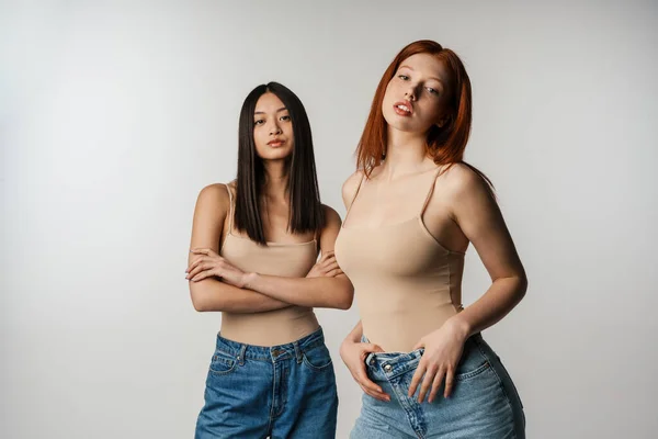 Duas Jovens Mulheres Multiétnicas Posando Juntas Sobre Fundo Parede Cinza — Fotografia de Stock
