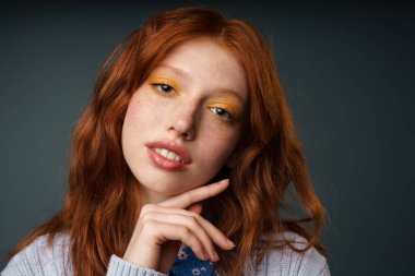 Gri arkaplanda izole edilmiş genç kızıl beyaz kadın poz veriyor ve kameraya bakıyor.