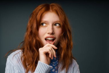 Genç kızıl, gri arka planda yalnız poz veren ve yan bakan kadını şaşırttı.