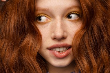 Makyajlı, genç, kızıl, beyaz bir kadın. İçeriye bakıyor.