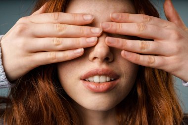 Genç, kızıl, beyaz bir kadın gri duvarın üzerinde poz veriyor ve gözlerini kapatıyor.