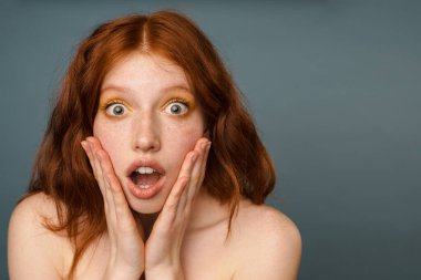 Gri arka planda izole edilmiş kameraya şaşırdığını belirten tişörtsüz kadın.