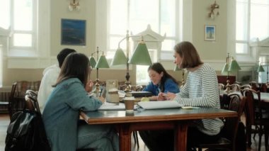 Bir grup genç öğrenci kütüphane salonunda masada oturup konuşuyorlar.