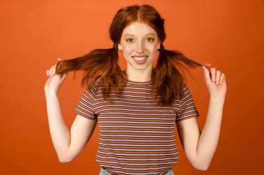 Kızıl saçlı, neşeli bir kadın turuncu arka planda saklanmış kuyruğuyla ve gülüşüyle dalga geçiyor.