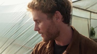 A close-up view of a farmer man talking while pointing to the fields standing between greenhouse outside