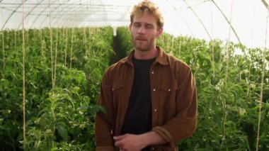 A confident farmer is standing at the greenhouse